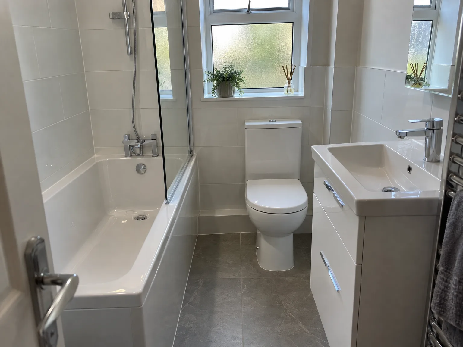 Modern fitted bathroom with white bath, toilet and vanity unit with slate floor tiles and natural light