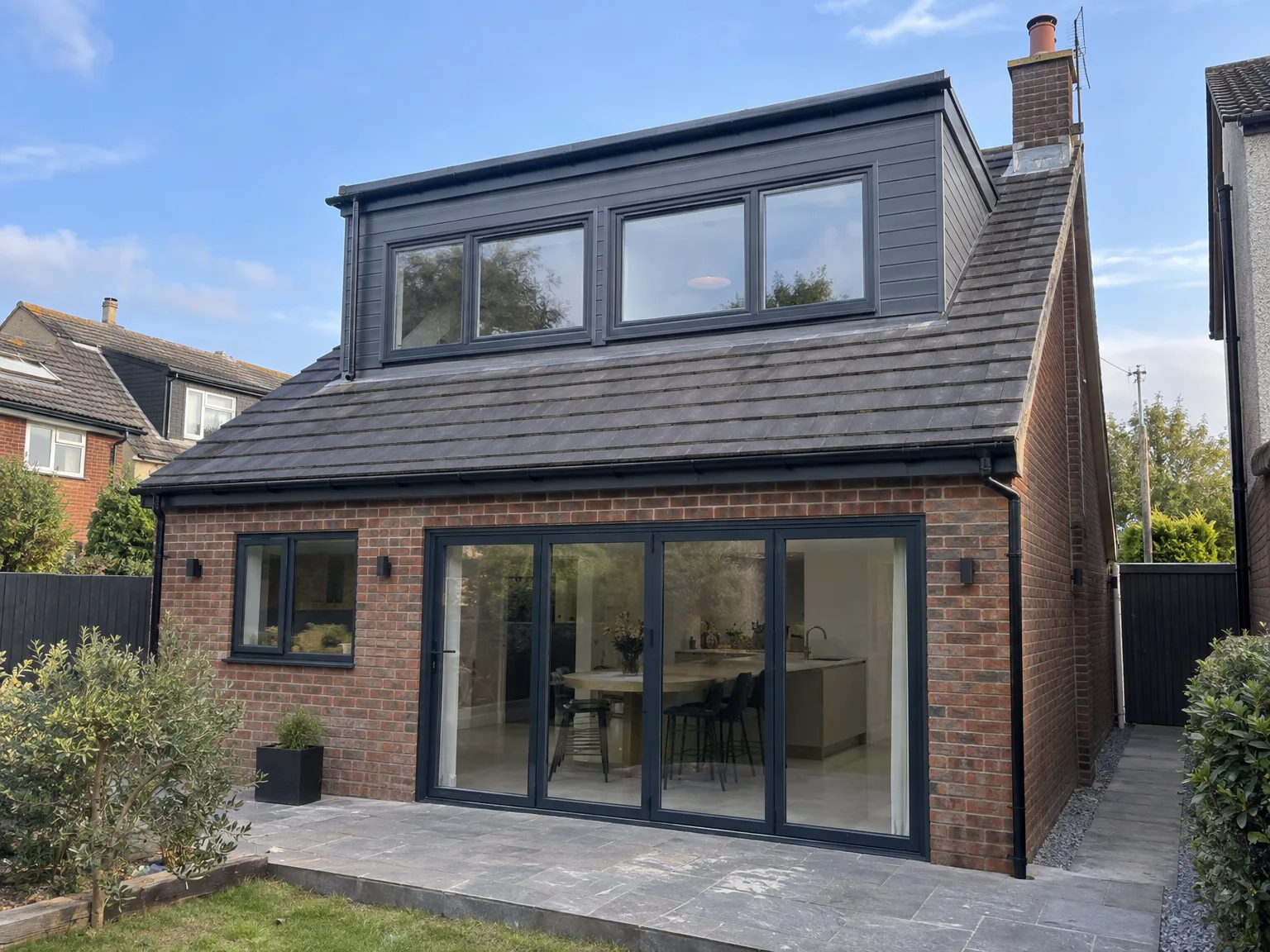 Contemporary two-storey house extension with grey timber cladding, red brick base, black-framed windows and bifold doors