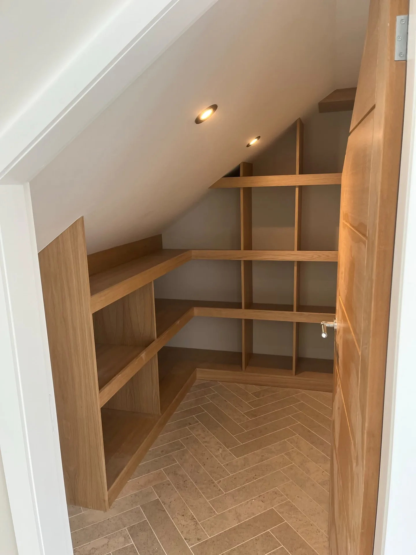 Fitted oak storage shelves and bespoke joinery in a converted loft space with herringbone flooring and LED lighting