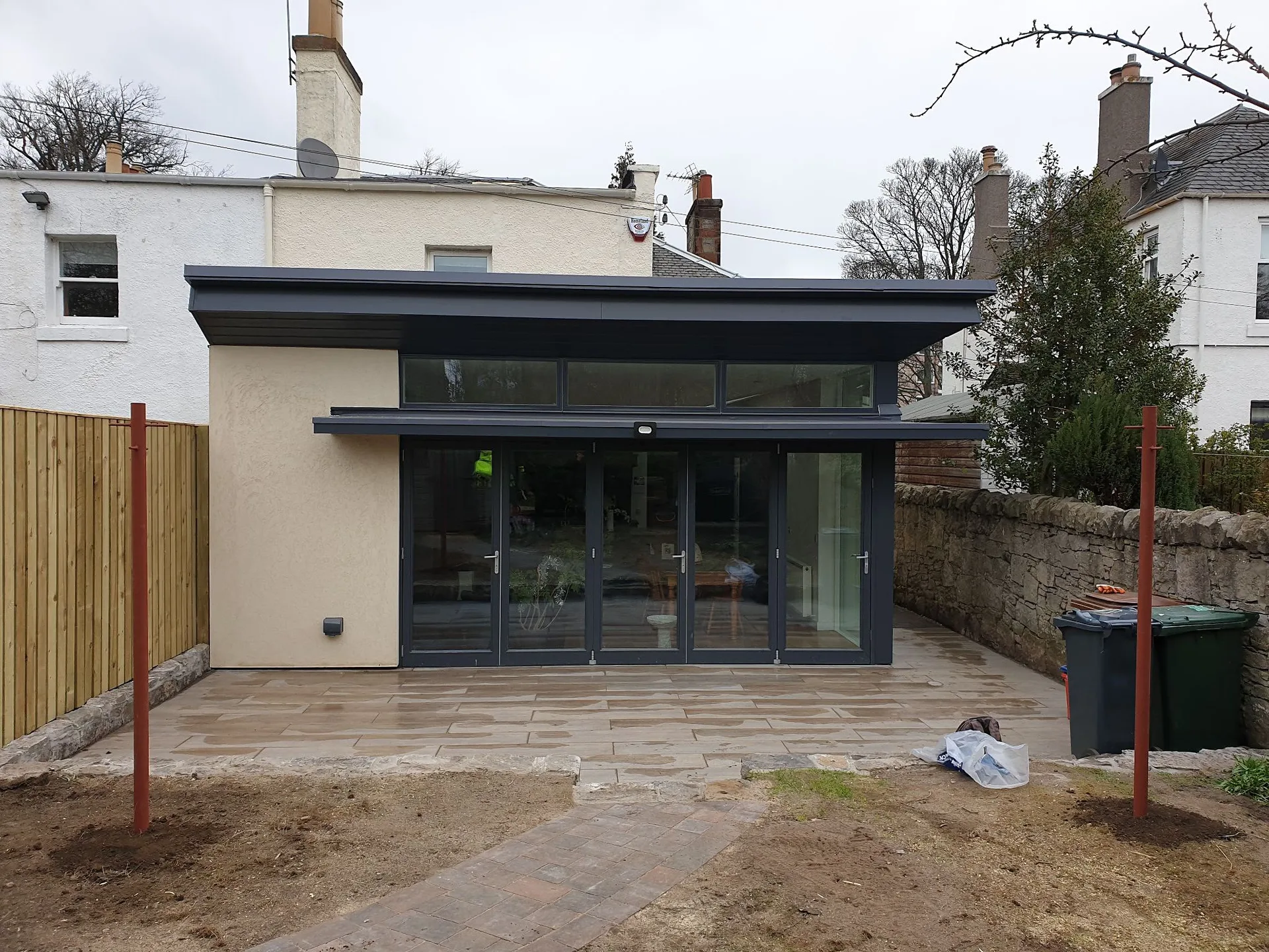 Modern black-framed house extension with patio flooring and wooden fence enclosure