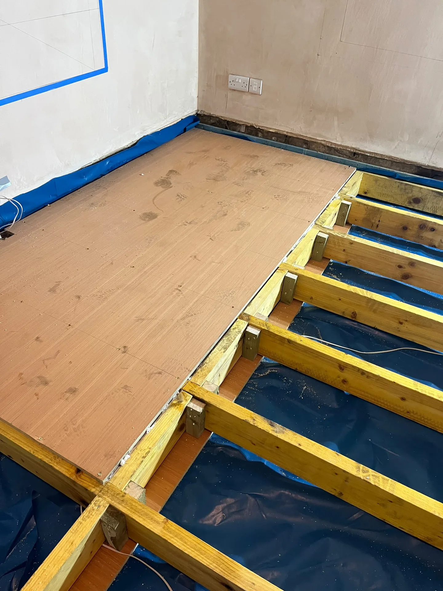 Wooden flooring laid with exposed yellow floor joists and taped drywall walls during interior renovation