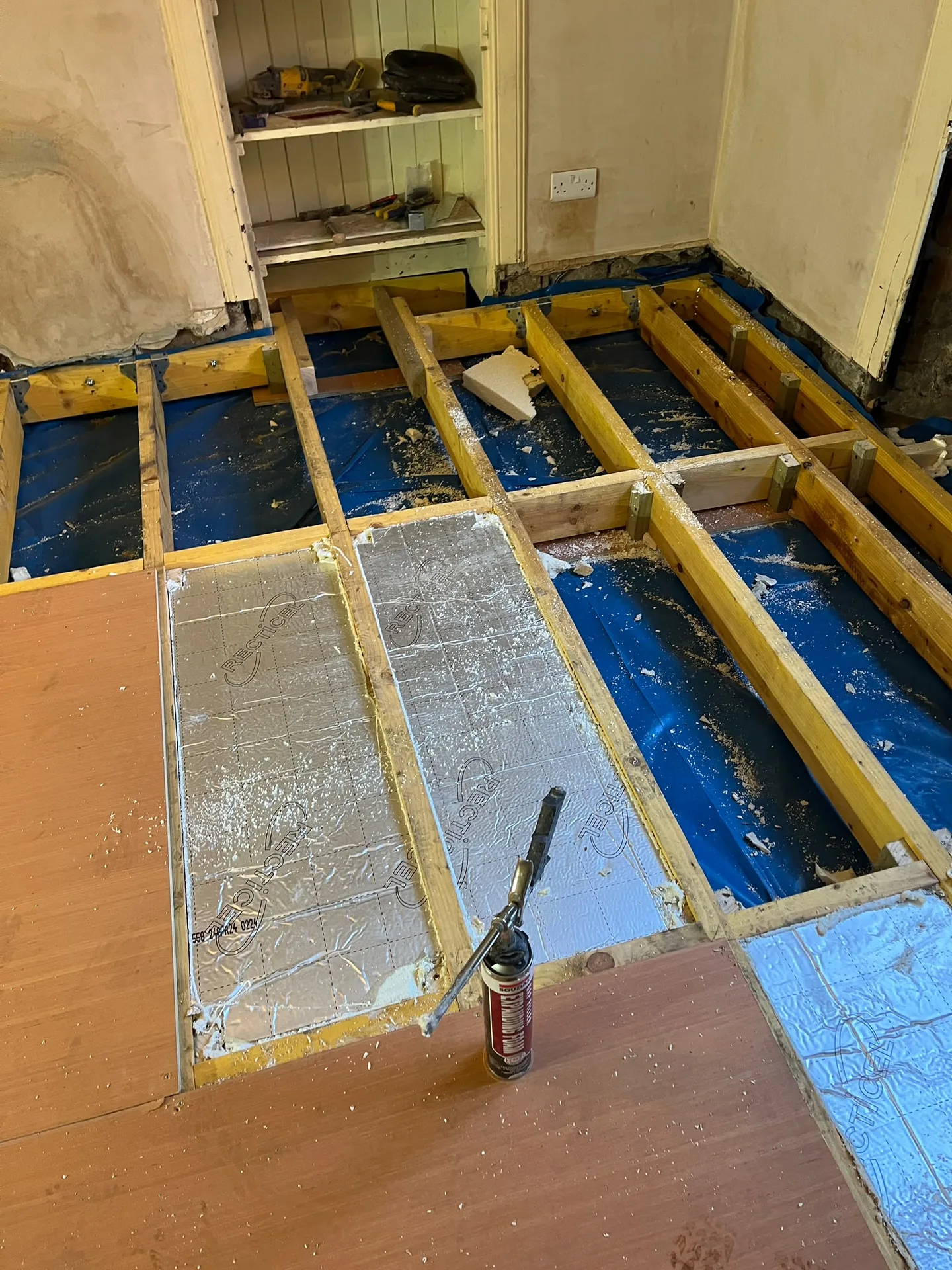 Interior renovation showing timber structural framing, wooden floor joists with blue damp-proof membrane protection