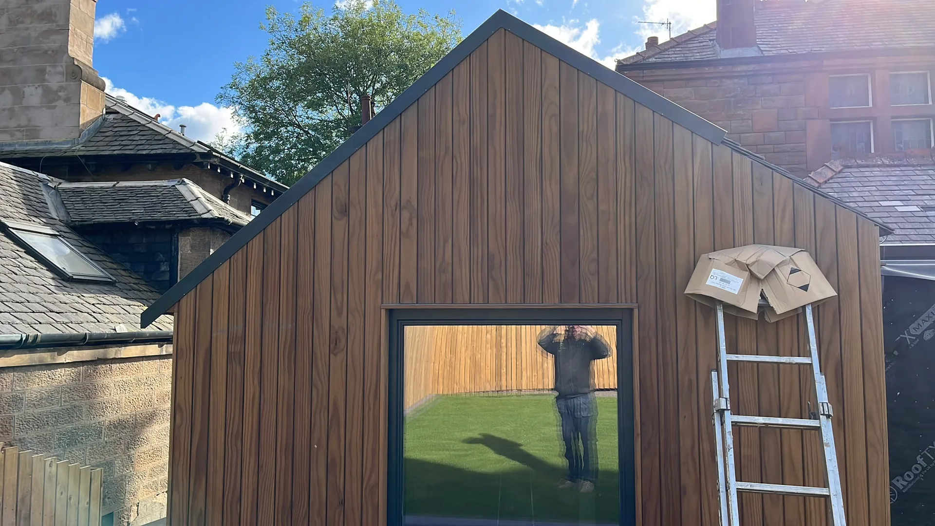 Wooden garden building with vertical timber cladding and large window, under construction