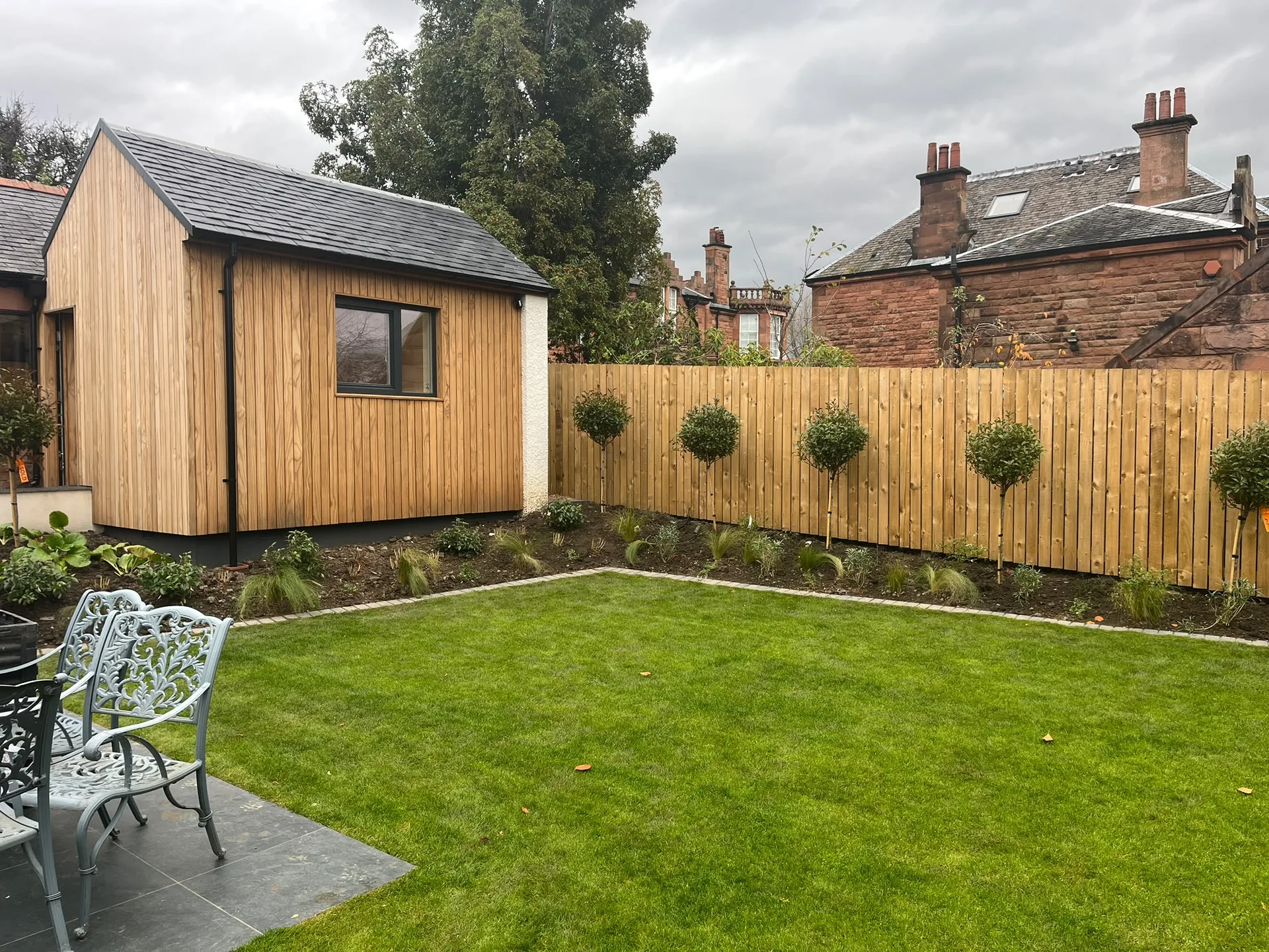 Wooden garden building with large window, pitched roof, timber fence and manicured lawn in residential garden