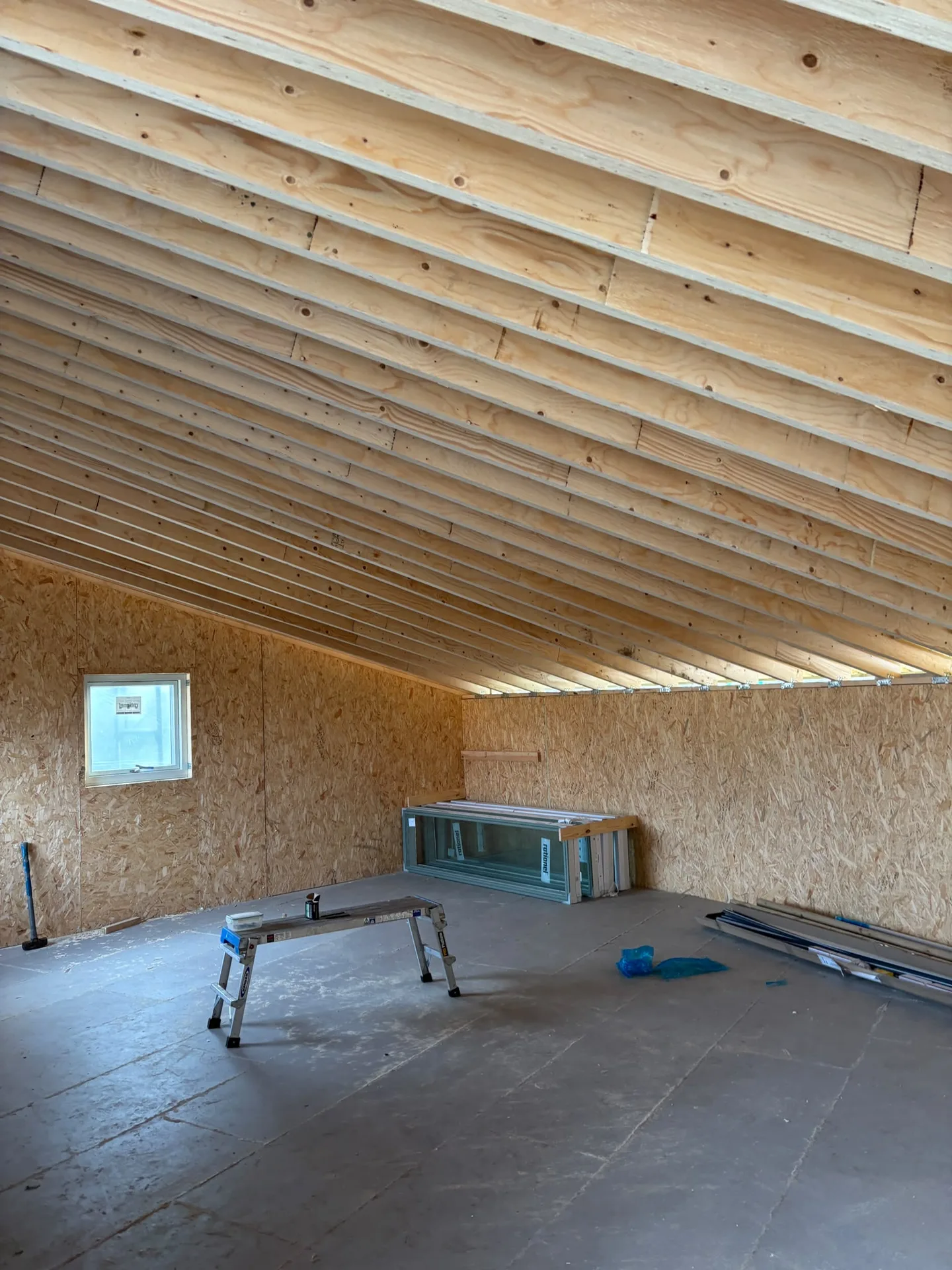 Loft conversion under construction showing wooden beam structure, boarded walls and concrete flooring