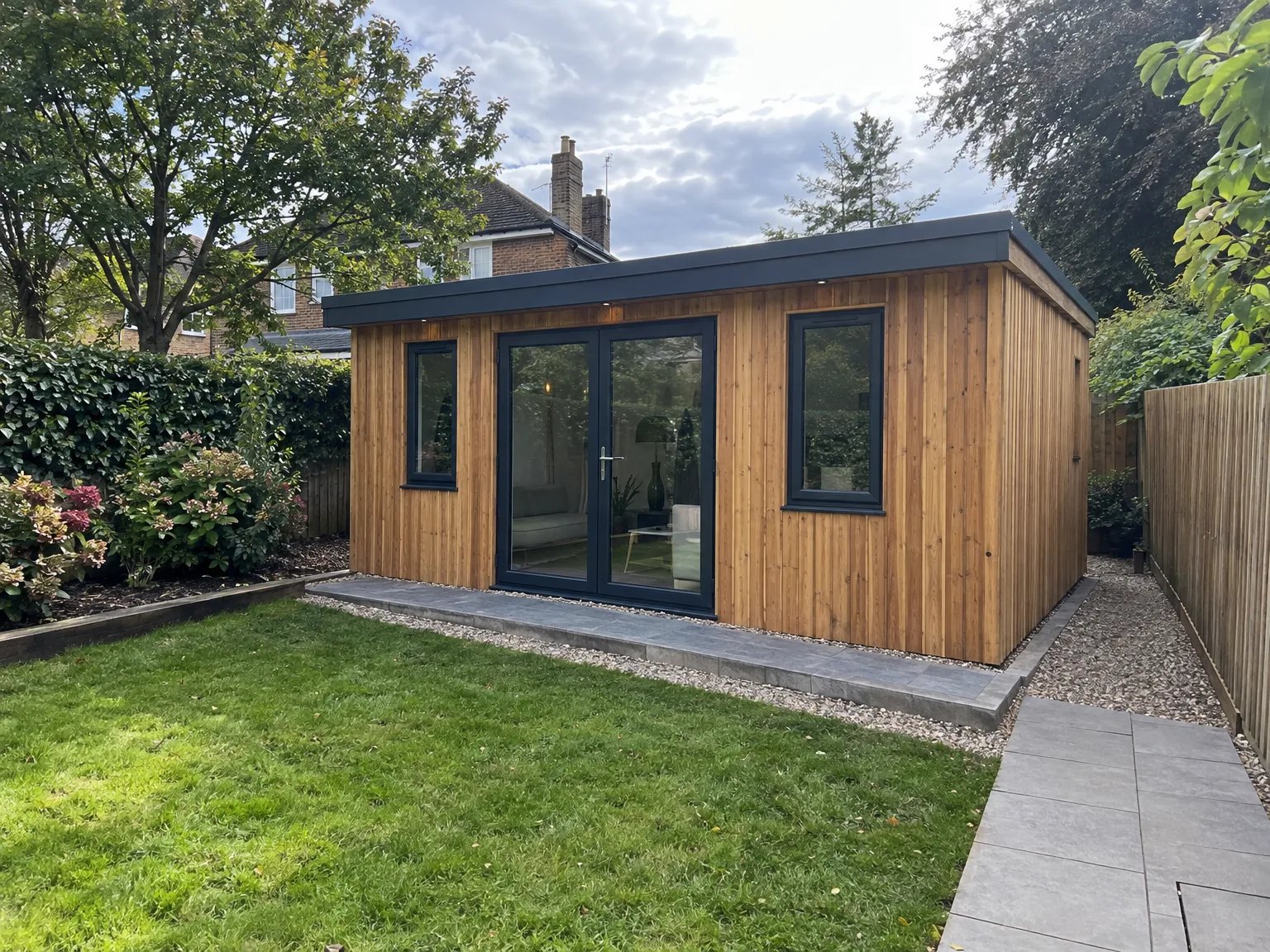 Modern garden room with timber cladding, black windows and stone patio in a residential garden