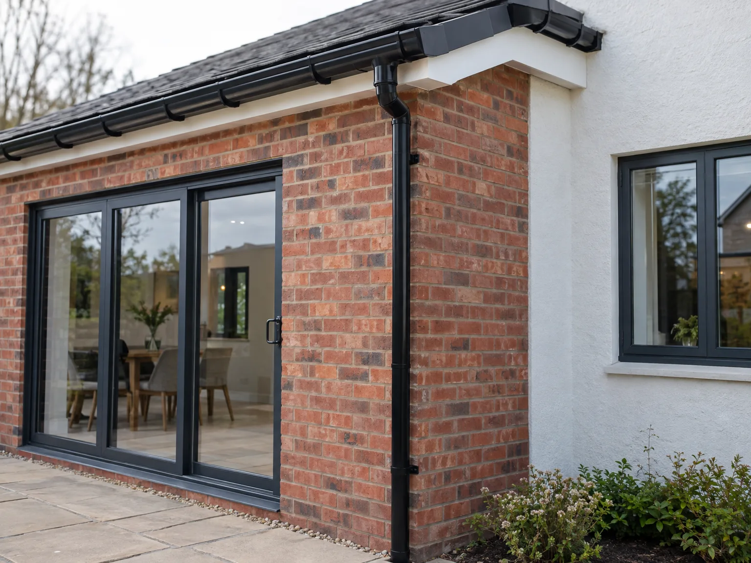 Black frame patio doors opening to brick house extension with new patio