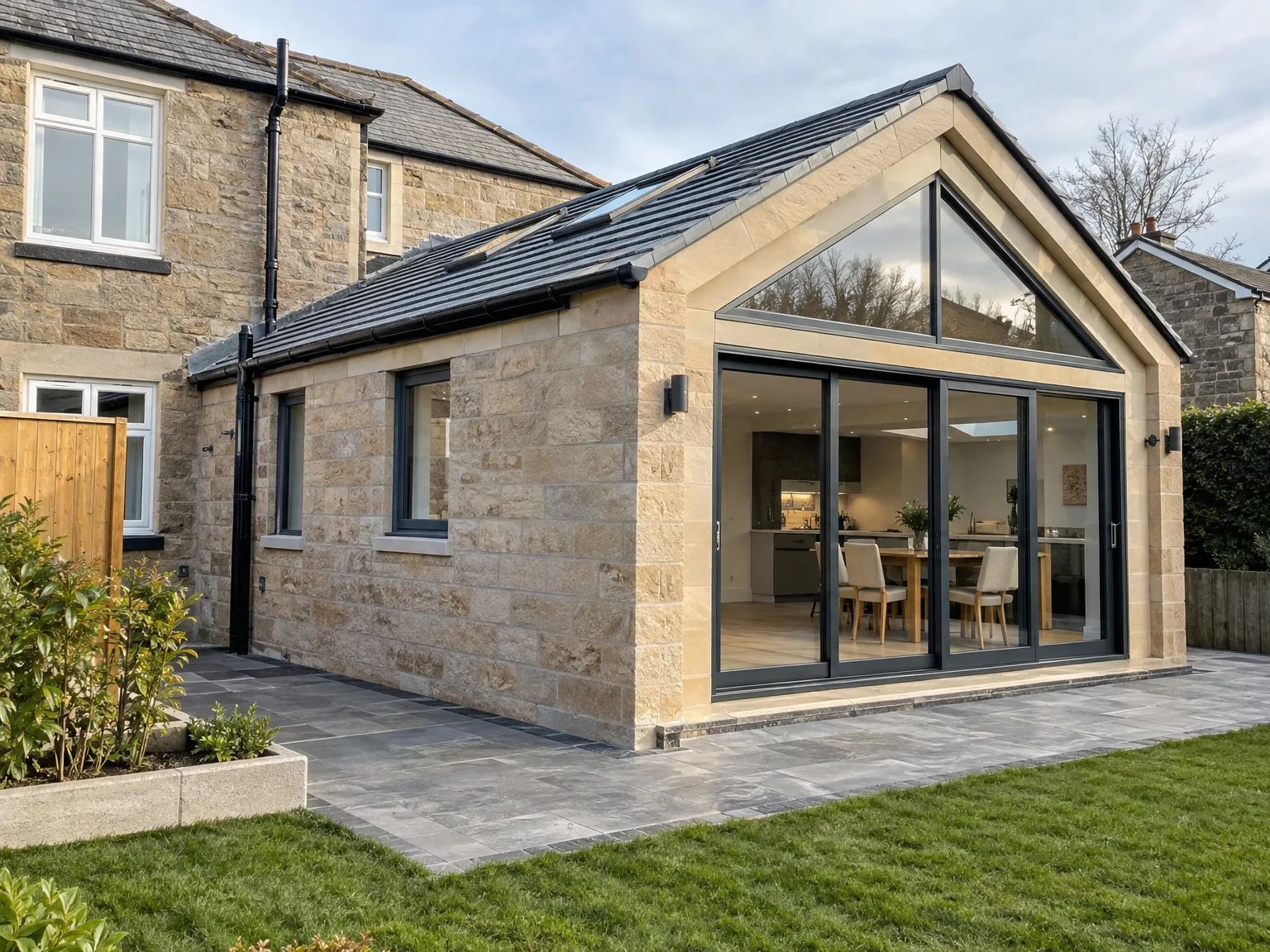 Modern stone house extension with large glazed doors opening onto slate patio, interior seating area visible inside