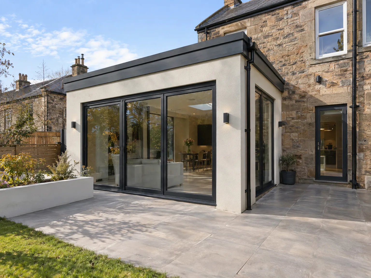 Modern house extension with large black-framed sliding glass doors and white render attached to traditional stone building