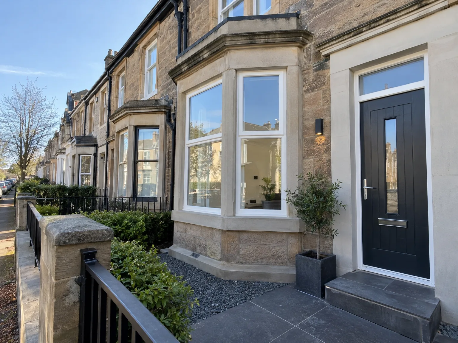 Renovated stone townhouse with bay windows, black entrance door and landscaped patio