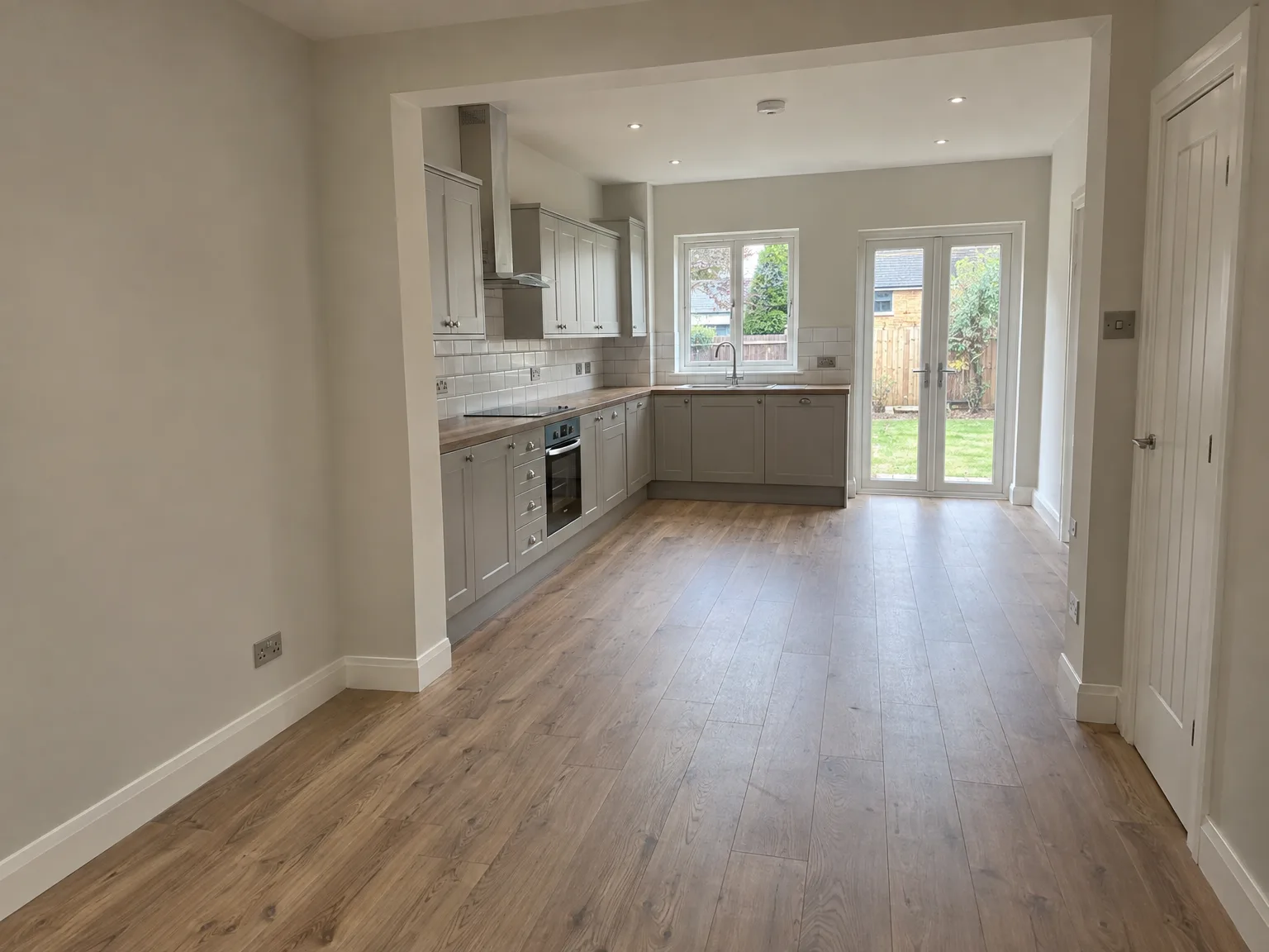 Modern fitted kitchen with grey cabinetry, wood flooring and patio doors overlooking garden
