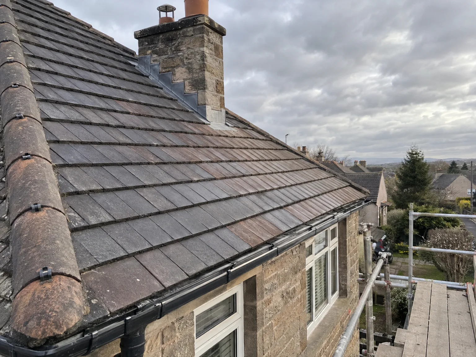 Professional slate roofing with stone chimney and modern metal guttering installation