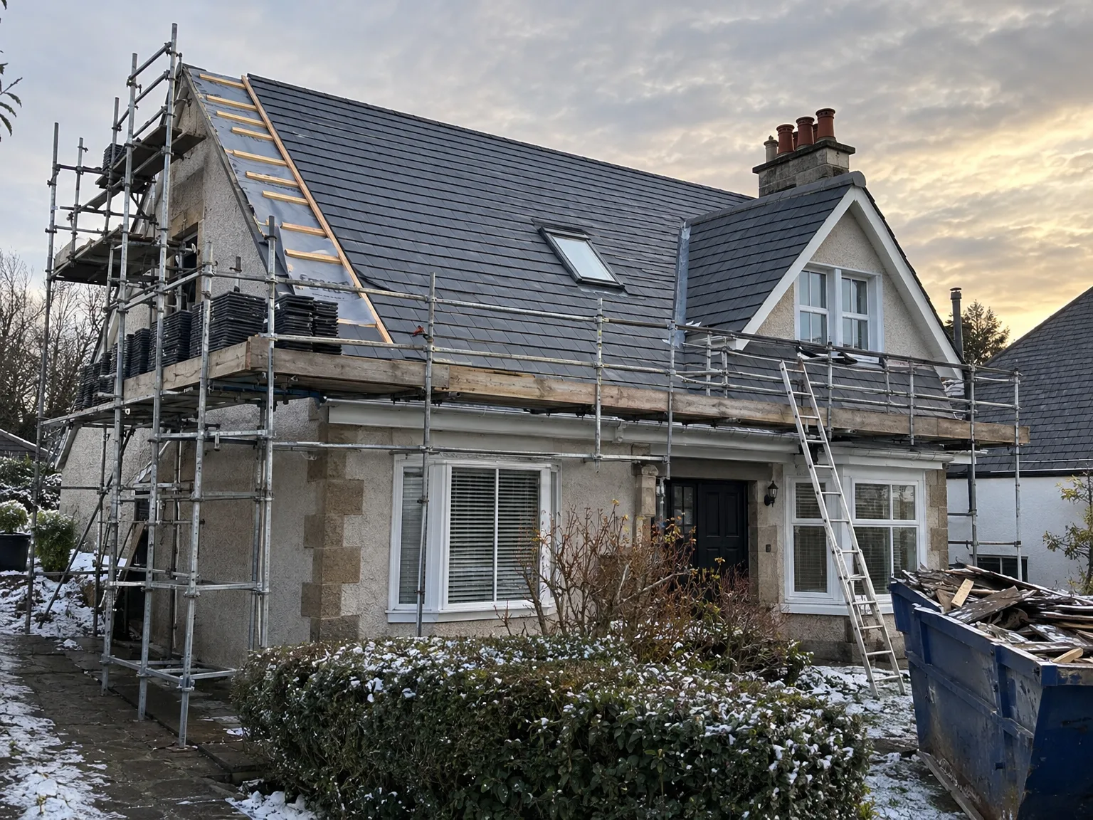 Roof replacement in progress on residential house with new slate tiles and temporary construction scaffolding