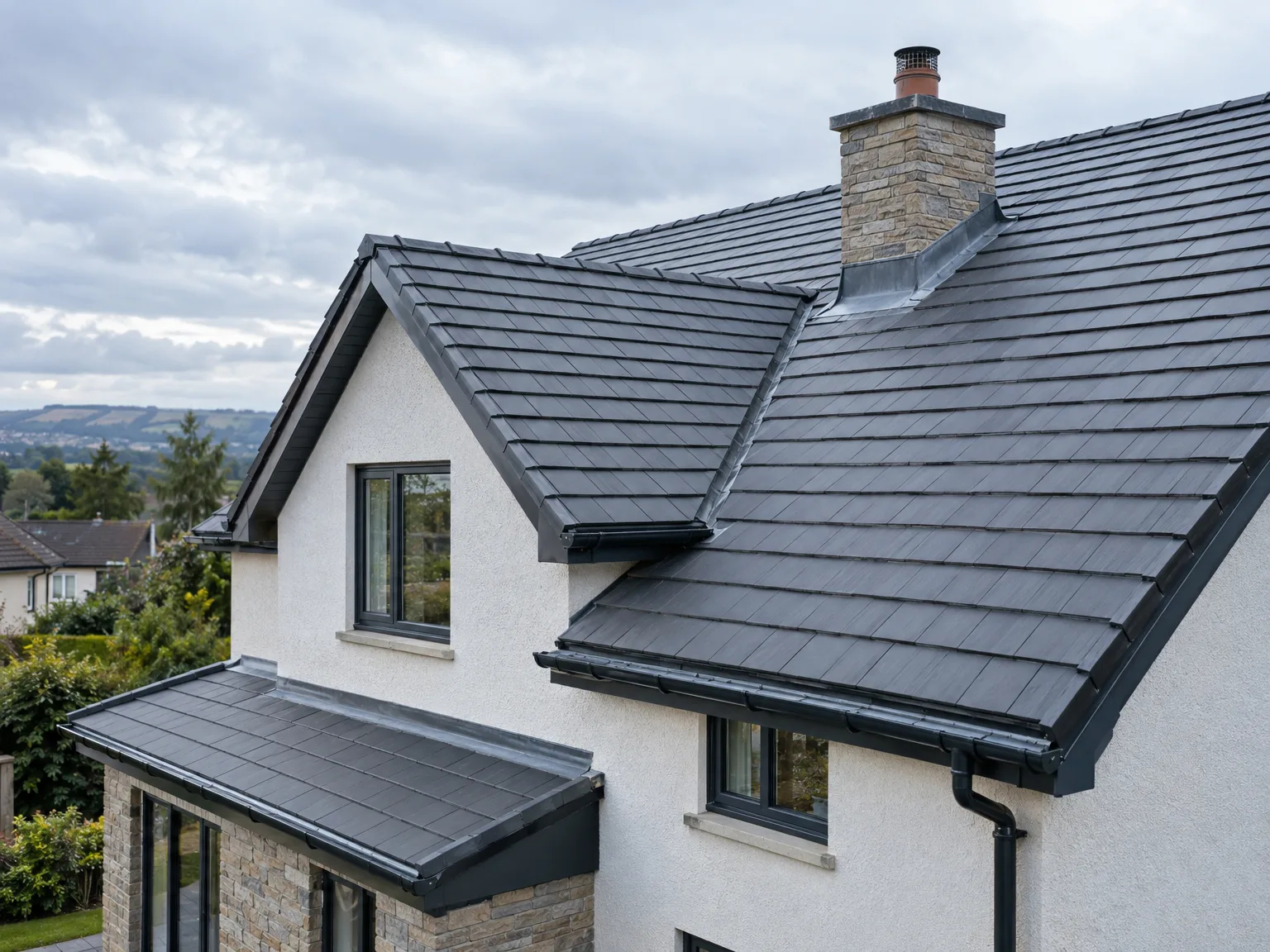 Slate pitched roof with stone chimney, dark tiles and rendered white walls overlooking countryside