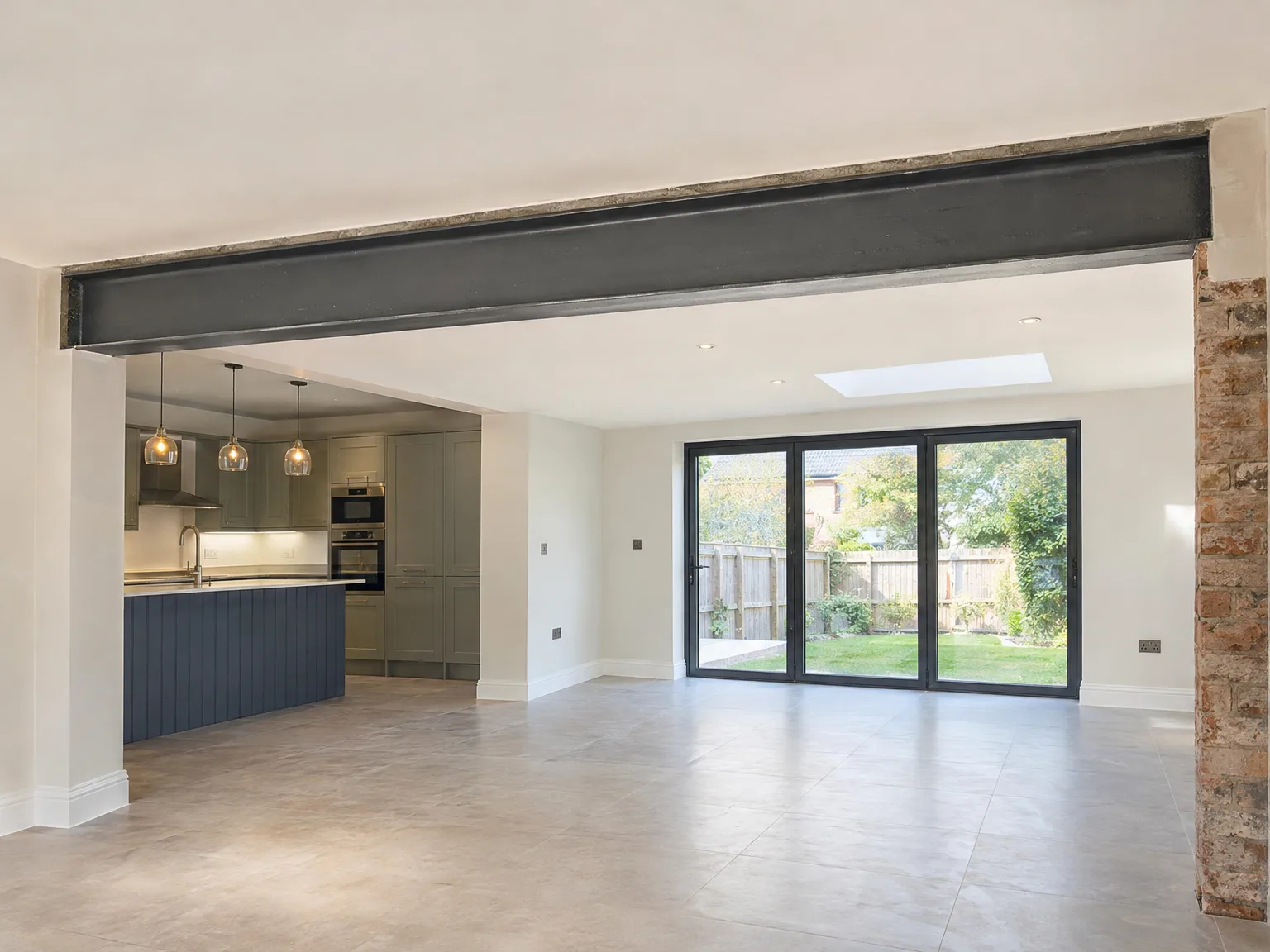 Modern open-plan kitchen and living extension with steel beam, kitchen island, and large bi-fold doors overlooking garden