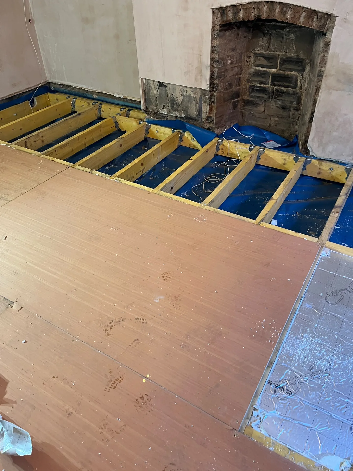 Wooden flooring installation with exposed timber joists and protective blue membrane during property renovation