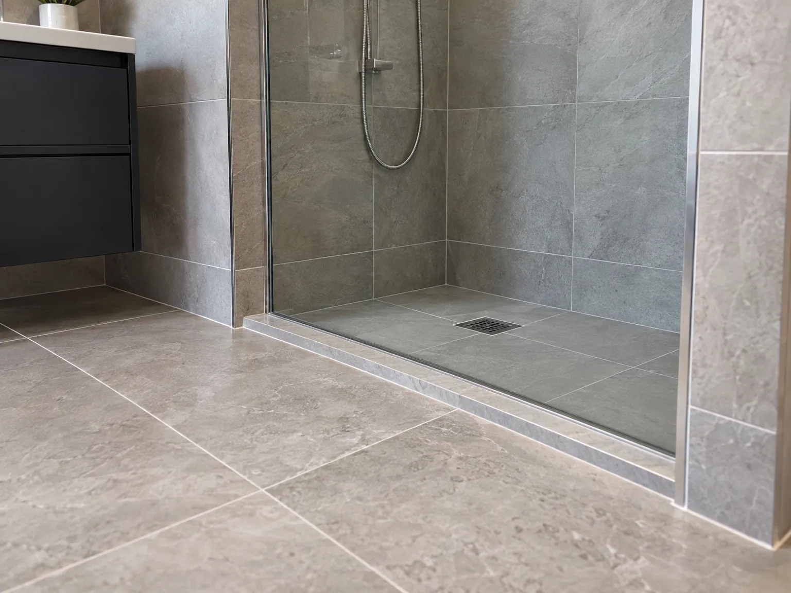 Modern bathroom with grey stone tile walk-in shower enclosure, chrome fixtures and neutral tone floor tiling. Bathroom Fitting and Tiling work