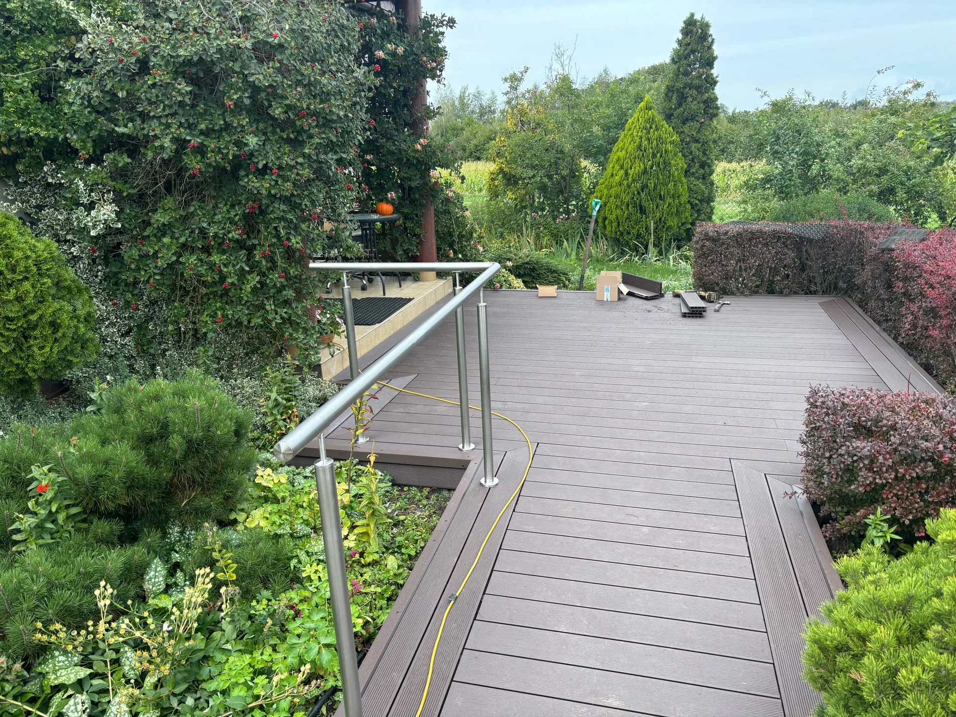 Wooden timber deck with metal railings, surrounded by a lush garden with mature plants and shrubs