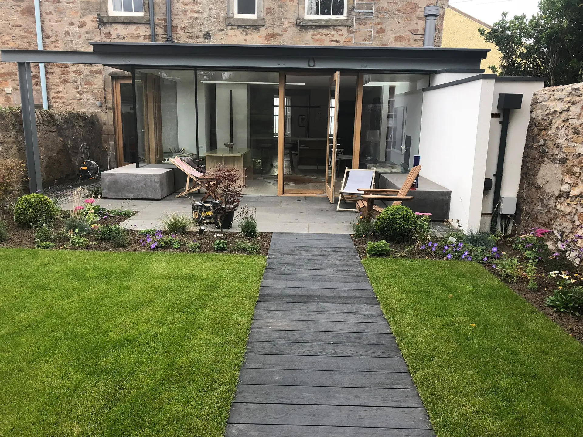Contemporary single-storey house extension with extensive glazing and timber decking to stone cottage